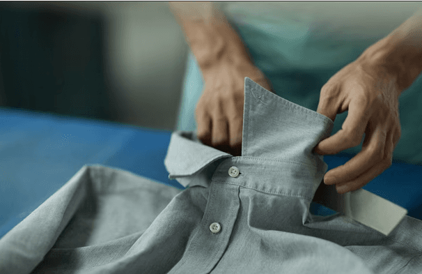 Person folding a gray button-up shirt.