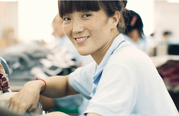 Woman smiling at the camera while sewing clothing.